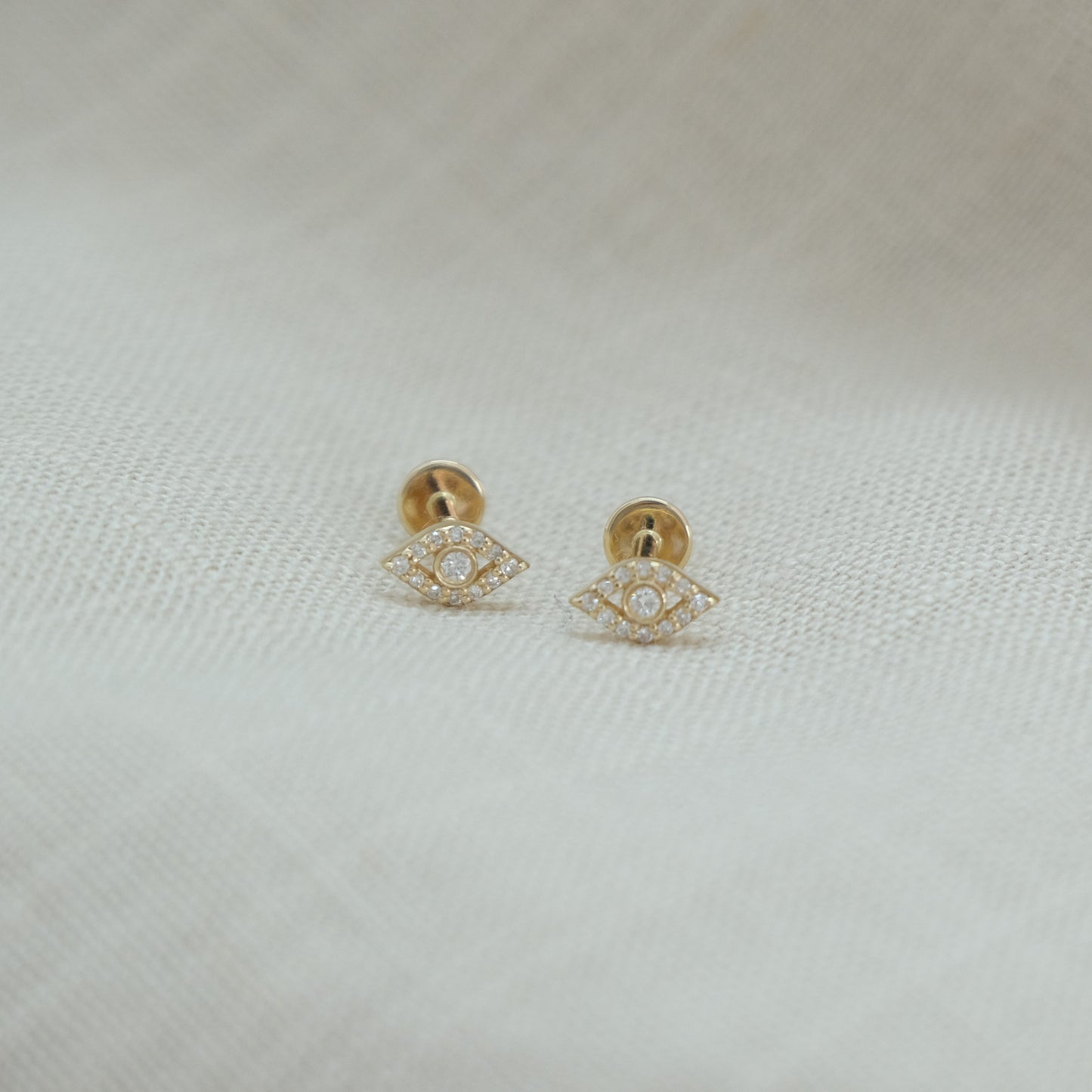 14ct recycled gold diamond evil eye studs on a beige linen background