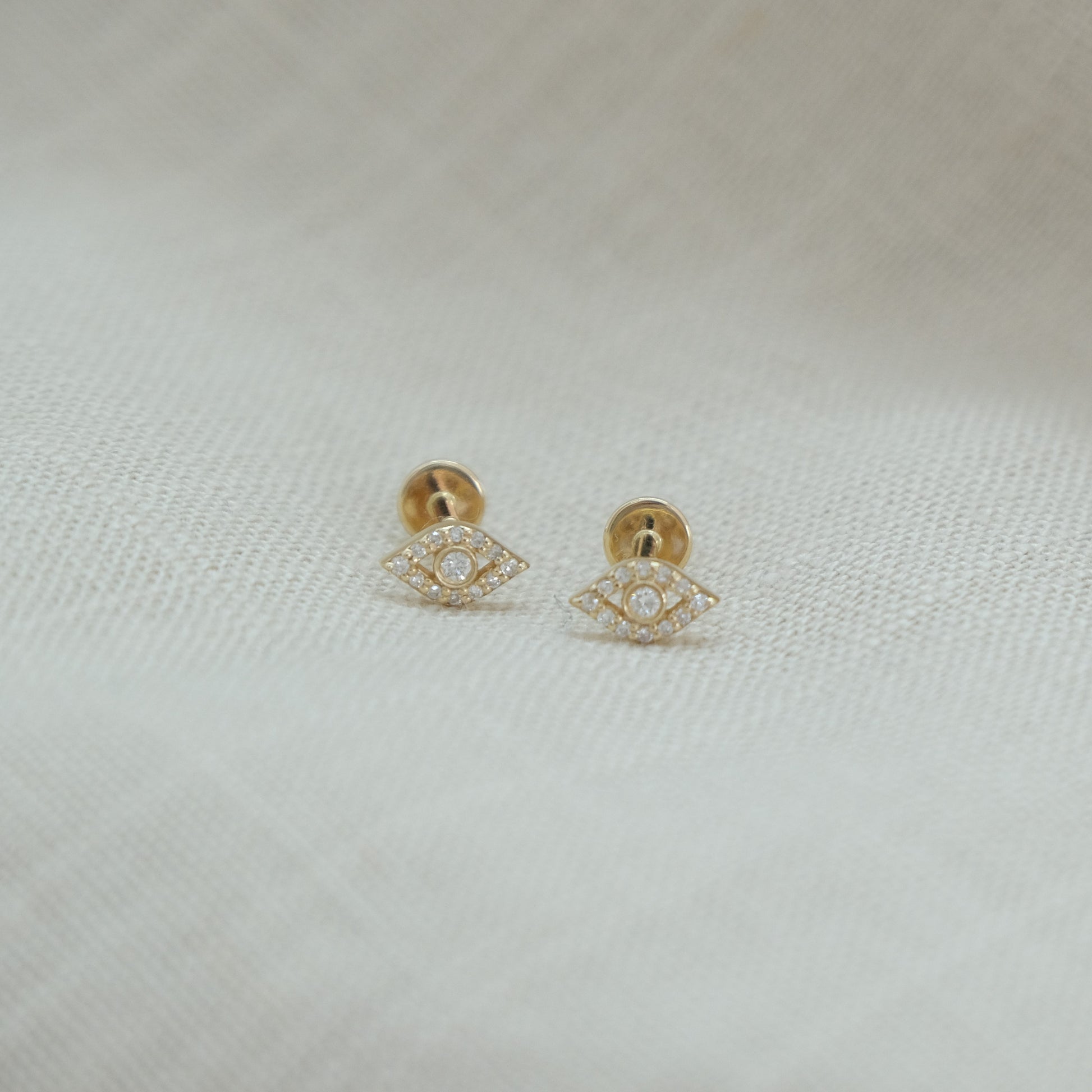 14ct recycled gold diamond evil eye studs on a beige linen background